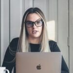 Frau mittleren Alters sitzt am Laptop und schaut irritiert auf eine Videokonferenz