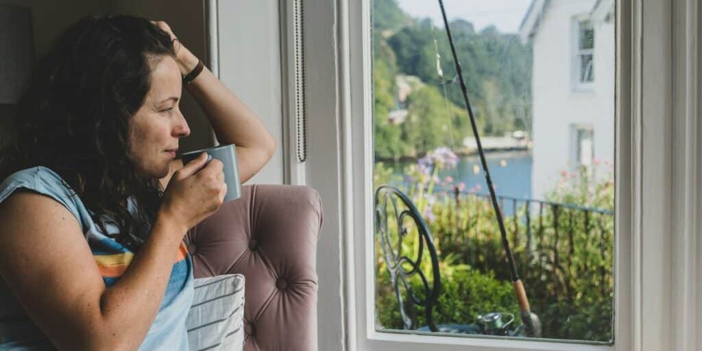 Nachdenkliche Frau mit Tasse am Fenster