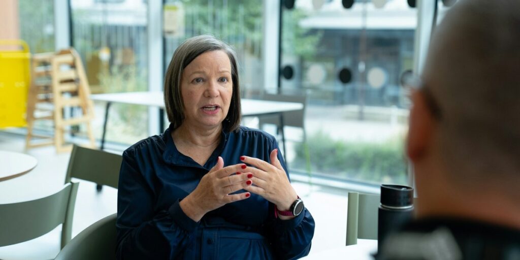 Frau in einer Gesprächsrunde stellt freundlich eine Frage, die anderen hören zu