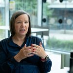 Frau in einer Gesprächsrunde stellt freundlich eine Frage, die anderen hören zu